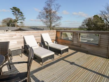 An outdoor wooden deck with two white cushioned lounge chairs and a wicker table and chairs at 1 Southern Place in Dobwalls