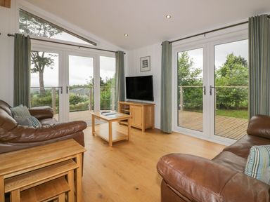 A living room with leather sofas wooden tables a television and large glass doors opening to a deck at 11 Faraway Fields Dobwalls