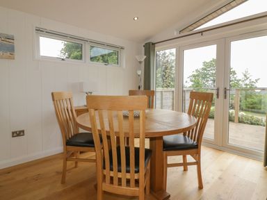 A dining area with a round wooden table and four chairs next to glass doors overlooking a deck at 11 Faraway Fields in Dobwalls