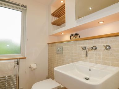 A bathroom with a wall-mounted sink toilet wooden shelves and frosted window at 11 Faraway Fields in Dobwalls