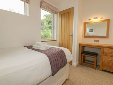A bedroom with a bed, desk, chair, mirror, window, and wooden door at 11 Faraway Fields in Dobwalls