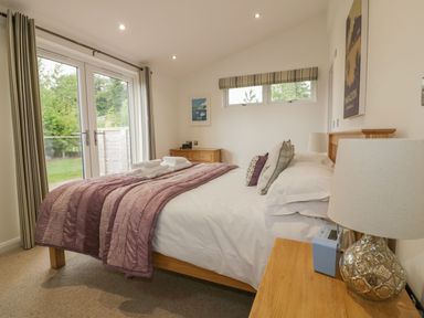A bedroom with a bed a bedside table lamp and glass doors leading to a garden at 11 Faraway Fields in Dobwalls