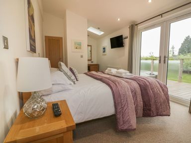 A bedroom with a bed covered in a pink blanket and pillows a bedside table with a lamp and remote and glass doors leading outside at 11 Faraway Fields in Dobwalls