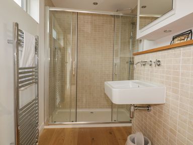A bathroom with a glass-enclosed shower a wall-mounted sink a towel rack with a white towel and a small trash bin at 11 Faraway Fields in Dobwalls
