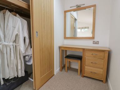 A wooden dressing table with a mirror above and a stool under next to a closet with white robes at 11 Faraway Fields in Dobwalls