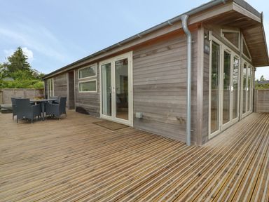 An outdoor wooden deck with a table and four chairs next to a building with glass doors at 11 Faraway Fields in Dobwalls