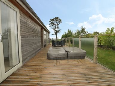 A wooden deck with a hot tub and outdoor table and chairs next to a house at 11 Faraway Fields in Dobwalls