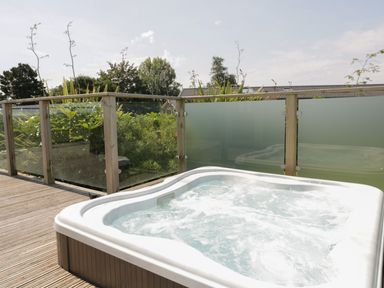 An outdoor hot tub on a wooden deck with glass panel railing and plants behind at 12 Faraway Fields in Dobwalls