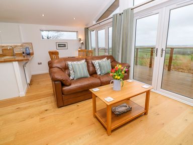 A living room with a brown leather sofa two pillows wooden coffee table with flowers and dining table with chairs at 12 Faraway Fields in Dobwalls