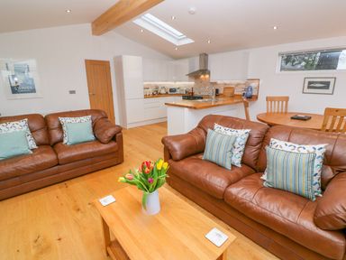 A living room with two brown leather sofas and a wooden coffee table with flowers at 12 Faraway Fields in Dobwalls