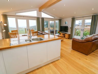 An open plan kitchen and living area with a wooden floor leather sofas dining table and large windows at 12 Faraway Fields in Dobwalls