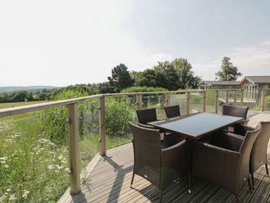 An outdoor deck area with a glass-top table and six wicker chairs surrounded by glass railing at 12 Faraway Fields in Dobwalls