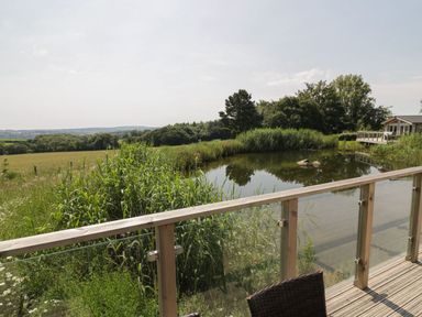 A wooden deck with glass railing overlooking a pond and green fields at 12 Faraway Fields in Dobwalls