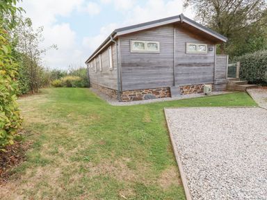 A wooden building with small windows surrounded by grass and gravel at 15 Faraway Fields in Dobwalls