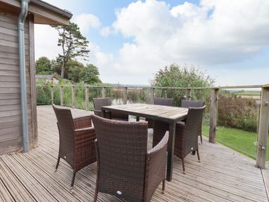 An outdoor deck with a wooden table and six wicker chairs surrounded by railing at 15 Faraway Fields in Dobwalls