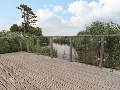 A wooden deck with glass panels overlooking a pond with reeds and trees at 15 Faraway Fields in Dobwalls