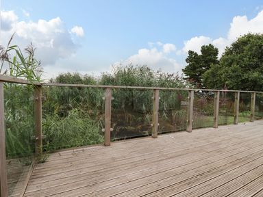 A wooden deck with glass and wooden railing overlooking green bushes and trees at 15 Faraway Fields in Dobwalls