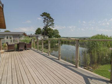 A wooden deck with outdoor furniture next to a pond and other houses visible in the background at 15 Faraway Fields in Dobwalls