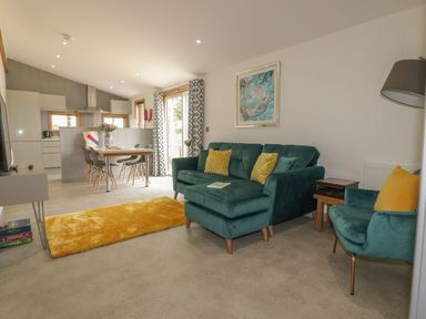 A living room with teal sofa and armchair with yellow cushions and dining table with chairs at 18 Meadow Retreat in Dobwalls