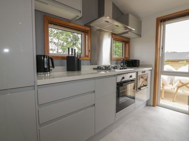 A kitchen with grey cabinets a gas stove an oven a knife block a kettle and a microwave next to windows and a door at 18 Meadow Retreat in Dobwalls