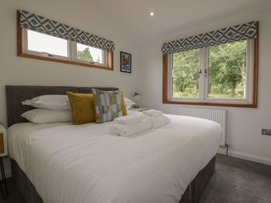 A bedroom with a double bed white bedding and pillows beside windows with patterned blinds at 18 Meadow Retreat in Dobwalls