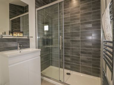 A bathroom with a white sink cabinet a glass shower enclosure with dark tiled walls and a heated towel rail at 18 Meadow Retreat in Dobwalls