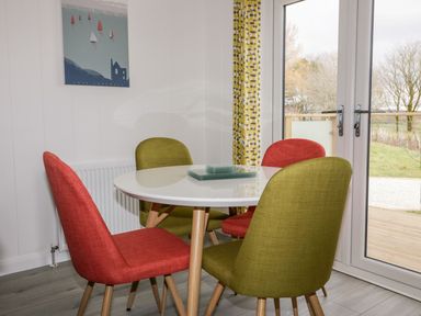 A dining area with a round white table and four chairs in red and green near glass doors at 11 Meadow Retreat in Dobwalls