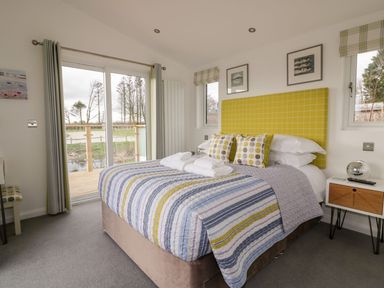 A bedroom with a double bed with striped bedding and yellow headboard at 11 Meadow Retreat in Dobwalls