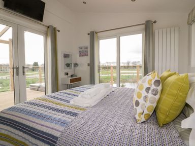 A bedroom with a bed with patterned pillows and blankets near sliding glass doors at 11 Meadow Retreat in Dobwalls