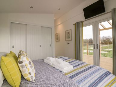 A bedroom with a bed covered with a striped and patterned bedspread and pillows next to sliding closet doors and glass doors leading to a deck at 11 Meadow Retreat in Dobwalls