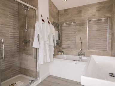 A bathroom with a shower enclosure two white robes hanging a bathtub and a sink at 11 Meadow Retreat in Dobwalls
