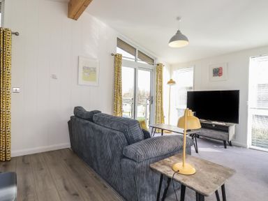 A living room with a gray sofa yellow lamps a television on a stand and glass doors with yellow patterned curtains at 11 Meadow Retreat in Dobwalls