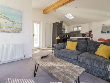 A living room with a grey sofa and yellow cushions and a kitchen area in the background at 11 Meadow Retreat Dobwalls