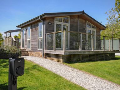 A wooden cabin with glass doors and a deck with metal chairs and table and a gravel path in front at 11 Meadow Retreat in Dobwalls