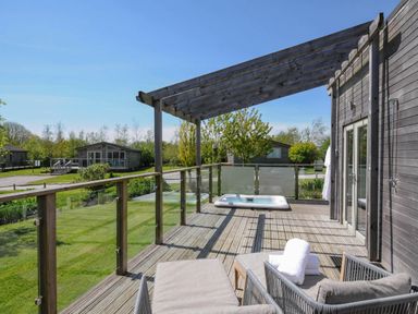 A wooden deck with lounge chairs a hot tub and glass railing overlooking a green lawn at 11 Meadow Retreat in Dobwalls