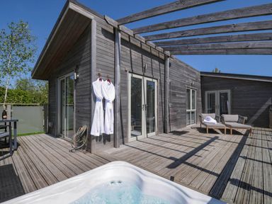 An outdoor wooden deck with two white bathrobes hanging on a wall a hot tub chairs and a table at 11 Meadow Retreat in Dobwalls