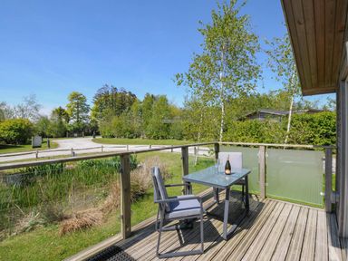 A wooden deck with a glass table and two chairs overlooking a grassy area and trees at 11 Meadow Retreat in Dobwalls