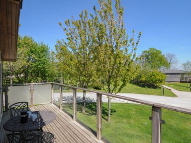 A balcony with a table and chairs overlooking trees and a grassy area at 11 Meadow Retreat in Dobwalls
