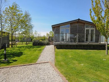 A wooden cabin with glass doors and a glass balcony railing surrounded by grass and trees at 11 Meadow Retreat in Dobwalls
