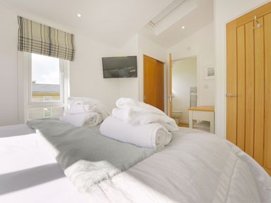 A bedroom with a bed and towels on it a window with striped blinds a television on the wall wooden doors and a desk with a chair at 4 Horizon View in Dobwalls