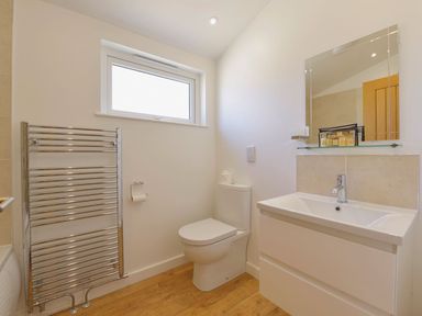 A bathroom with a toilet, sink with mirror, towel radiator, and wooden floor at 4 Horizon View in Dobwalls