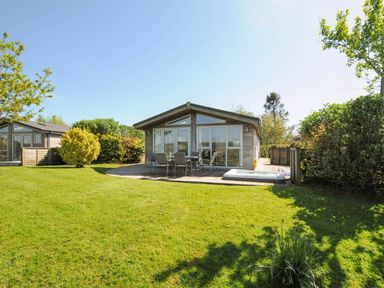 A wooden cabin with outdoor dining furniture and a hot tub on a deck surrounded by grass and trees at 4 Horizon View in Dobwalls