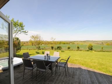 An outdoor wooden deck with a dining table and six chairs overlooking a green field at 4 Horizon View in Dobwalls