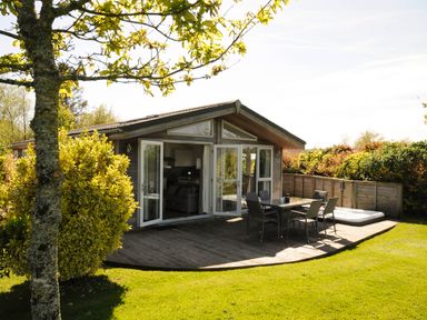 A wooden house with open doors leading to a patio with table and chairs and a hot tub in a garden at 4 Horizon View in Dobwalls