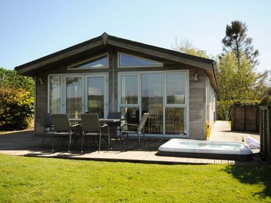 A wooden cabin with outdoor dining table chairs and a hot tub on a deck at 4 Horizon View in Dobwalls