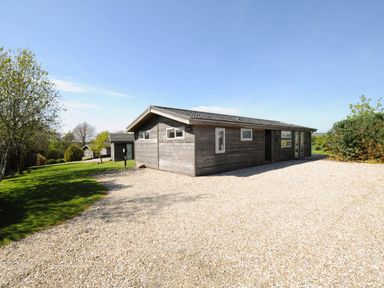 A wooden house with small windows and a gravel driveway surrounded by grass and trees at 4 Horizon View in Dobwalls