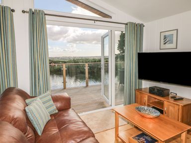 A living room with leather sofa and striped curtains opening to a deck overlooking water at 14 Faraway Fields in Dobwalls