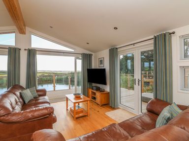 A living room with leather sofas coffee table and a TV with a view of a deck and countryside at 14 Faraway Fields in Dobwalls
