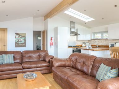 A living area with brown leather sofas and a wooden coffee table next to a kitchen with white cabinets and wooden countertops at 14 Faraway Fields in Dobwalls