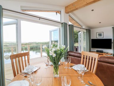 A dining table with place settings and flowers next to a living room with a leather sofa and a TV at 14 Faraway Fields in Dobwalls